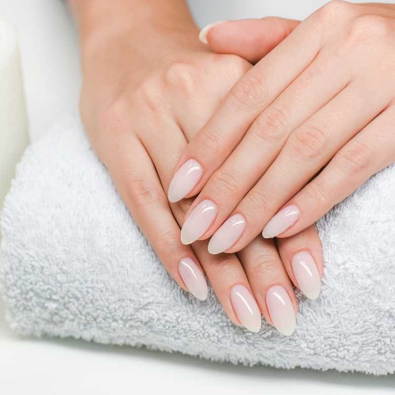 Woman's hands with white nail polish holding a towel, promoting tips for thicker hair and stronger nails.