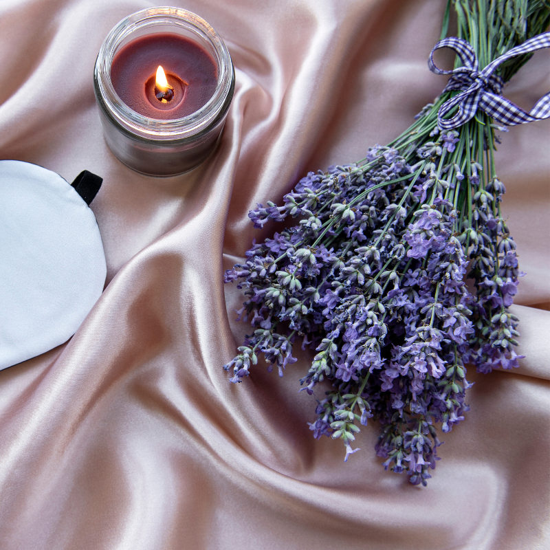 Lavender flowers and a candle on a silk sheet, promoting natural sleep improvement.