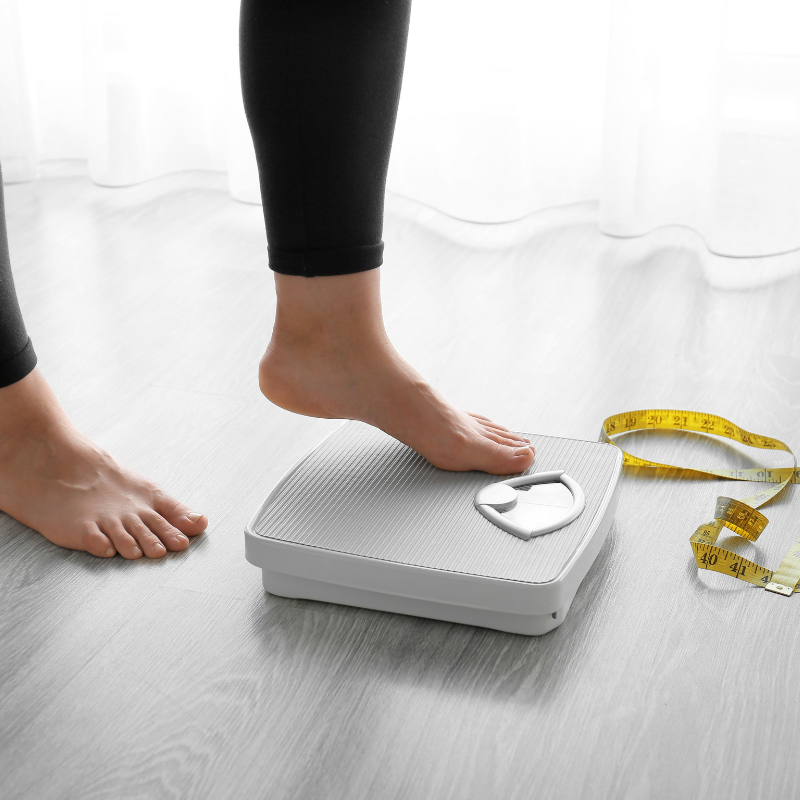 Woman standing on scale with tape measure, symbolizing weight loss journey.