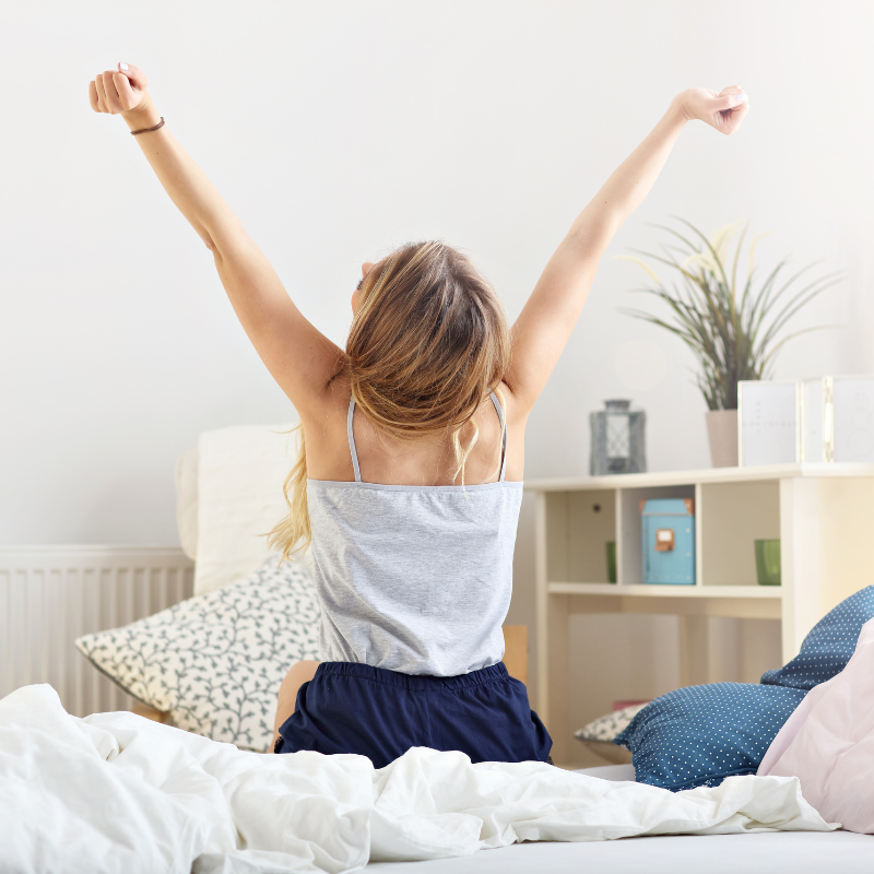 A woman sitting on her bed with her arms up, feeling energized by 6 herbs that provide more energy than coffee.