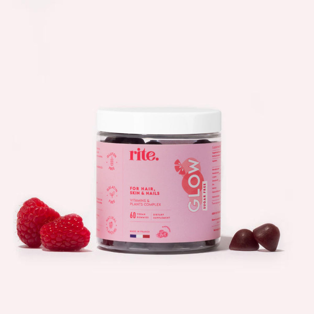 A jar of Rite GLOW Vitamin Gummies sits on a white surface next to a pile of red raspberries.
