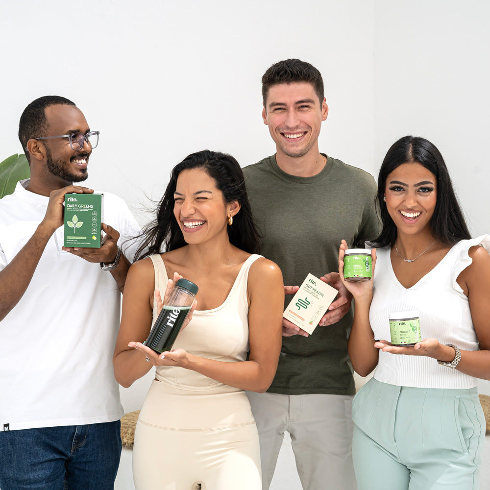 A diverse group of four people smiling and holding various health products, including a jar, boxes, and a tumbler, standing together against a light background.







