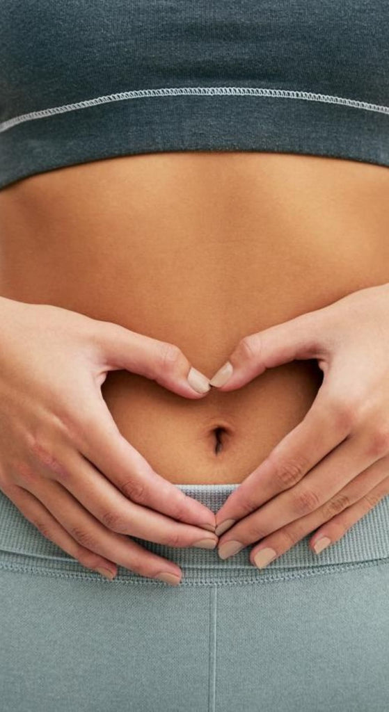 Close-up of a healthy belly with hands forming a heart shape, symbolizing digestive wellness from GLOW AND BALANCE GUMMIES