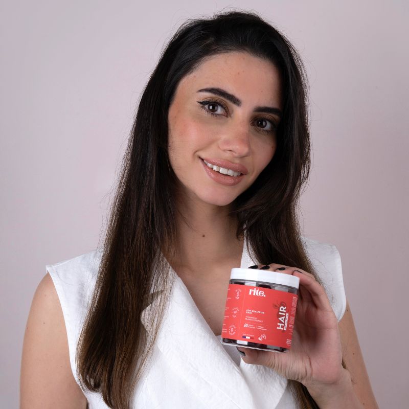 A woman with long hair holds a jar of hair care product labeled "HAIR Gummies" for healthier hair.