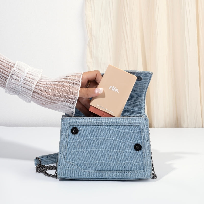 Hand placing a Rite. GUMMIES DISPENSER into a blue denim handbag, ideal for carrying supplements conveniently on the go.
