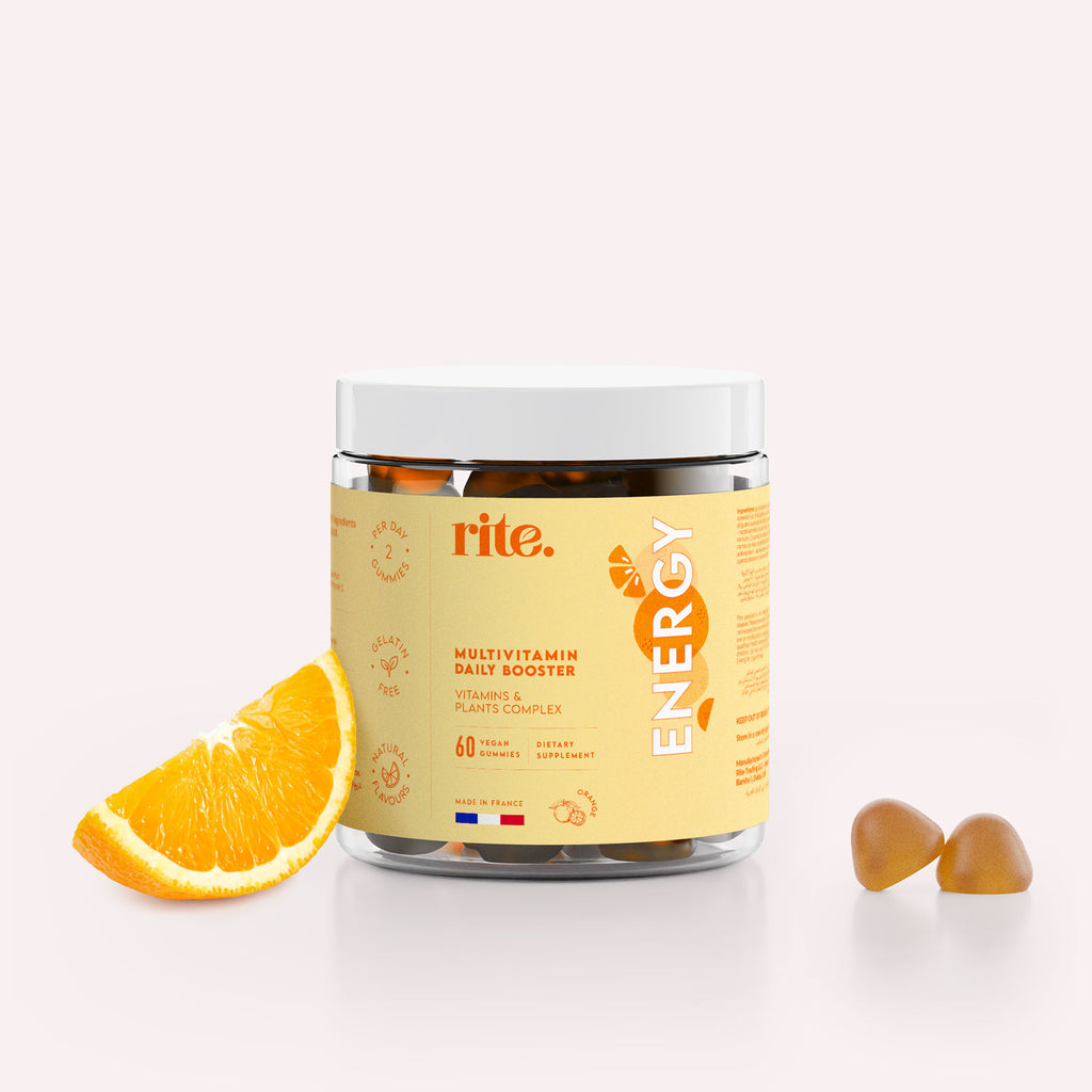 A jar of Rite ENERGY Vegan Gummies sits on a surface next to an orange slice. 