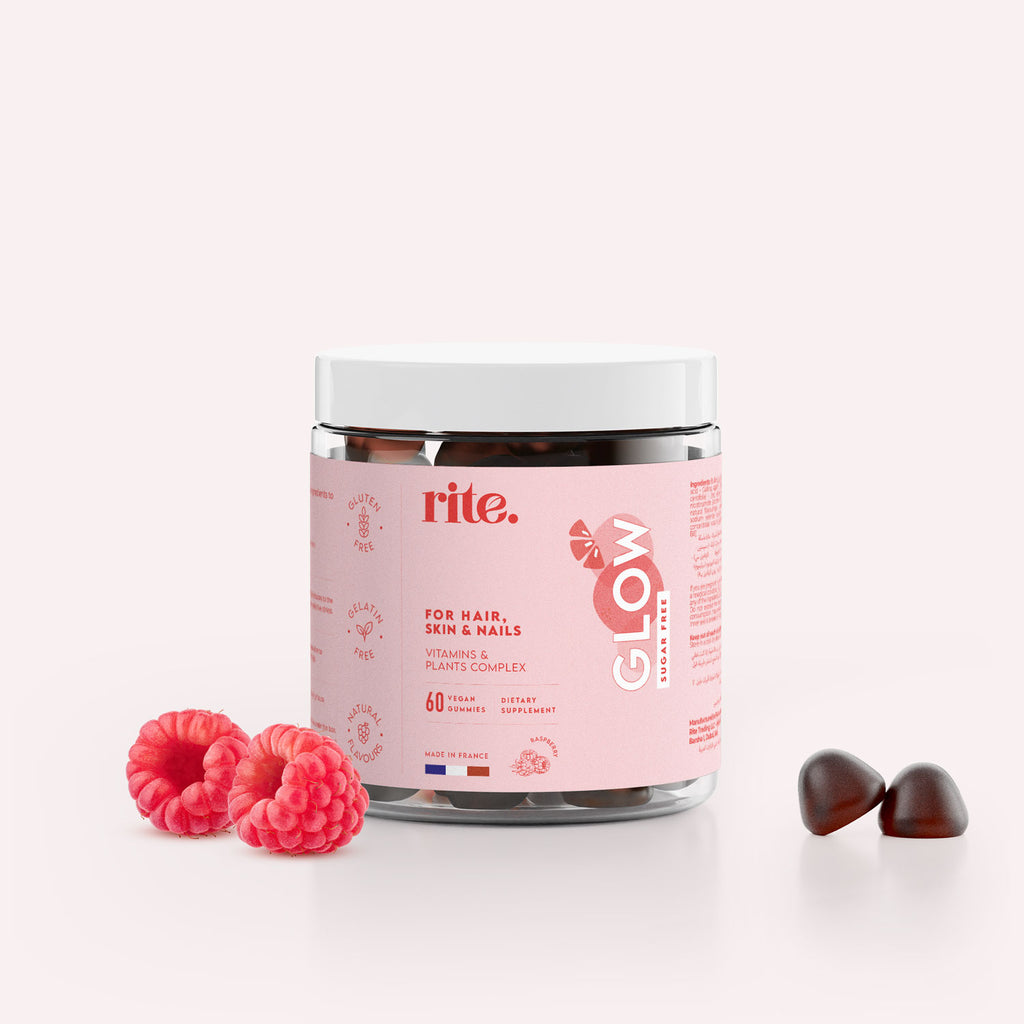 A jar of Rite GLOW Vitamin Gummies sits on a white surface next to a pile of red raspberries