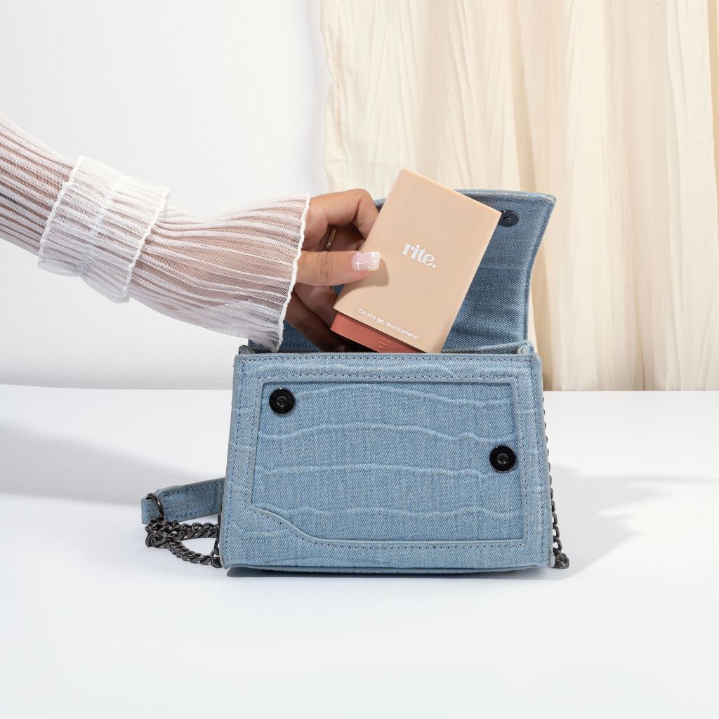 Hand placing a Rite. GUMMIES DISPENSER into a blue denim handbag, ideal for carrying supplements conveniently on the go.