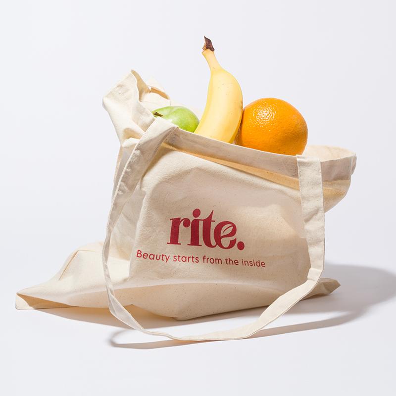 A reusable tote bag filled with colorful fruit sits on a white surface. 