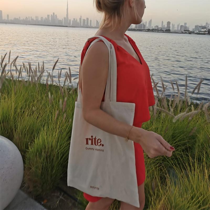 Woman walking by the waterfront at sunset with a tote bag advertising gummy vitamins.